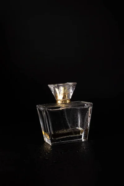A bottle of women\'s perfume on a black background with water drops. beauty and style concept