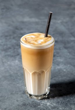 Kremalı ve sütlü buzlu bir bardakta buzlu kahve ve fotokopi alanı olan gri arka planda saman..