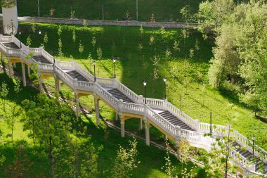 Lambalı taş bir merdiven, güneşli bir günde ağaçlı yeşil bir sokak boyunca yol açar.