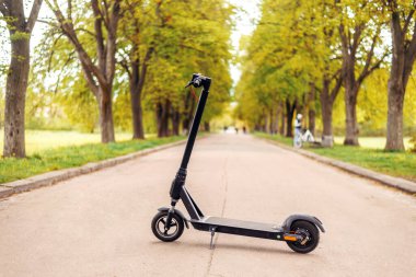 Parkta elektrikli scooter. Turuncu yol üzerinde yeşil ağaçlar arasında dolaşır. Modern eko-taşıma. Çevre kaygısı