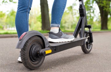Yazın arka planda elektrikli scooter 'ın üzerinde duran kadın bacaklarını kapat..
