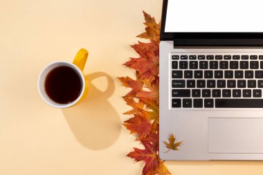 Kırmızı ve sarı yapraklı çalışma alanı, dizüstü bilgisayar, gölgeli bir fincan çay. Samimi ofis bej masasının üst manzarası. Sonbahar arkaplanı, düz uzanma