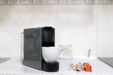 Modern kapsül kahve makinesi beyaz bir fincanda espresso yapıyor. Mutfak tezgahında dağınık kahve kapsülleri var. Yüksek kalite fotoğraf