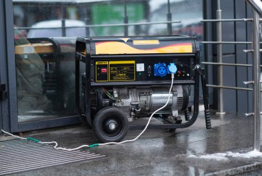 Yağmurlu bir kış gününde bir mağazanın dışında çalışan taşınabilir siyah benzin jeneratörüyle bağlı güç kabloları..