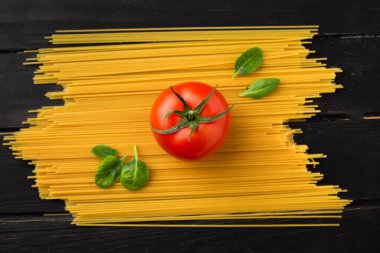 Siyah ahşap zemin üzerinde taze kırmızı domates ve yeşil ıspanak yapraklı çiğ spagetti makarna manzarası. İtalyan gıda konsepti