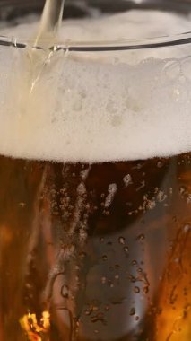 Kalın beyaz köpüklü ve yükselen köpüklü bir bardağa taze altın bira dökülüyor.