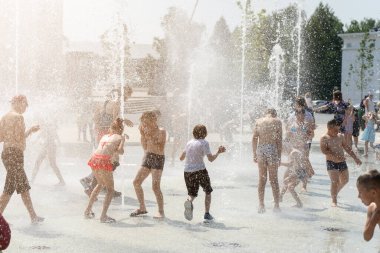 İzhevsk, Rusya - 20 Temmuz 2020: Mutlu çocuklar yaz parkındaki çeşmeye gülüp sıçrıyor. Bir grup çocuk şehir çeşmesinin derelerinde eğleniyor.