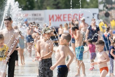İzhevsk, Rusya - 20 Temmuz 2020: Mutlu çocuklar yaz parkındaki çeşmeye gülüp sıçrıyor. Bir grup çocuk şehir çeşmesinin derelerinde eğleniyor.