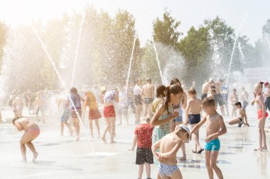 İzhevsk, Rusya - 20 Temmuz 2020: Mutlu çocuklar yaz parkındaki çeşmeye gülüp sıçrıyor. Bir grup çocuk şehir çeşmesinin derelerinde eğleniyor.