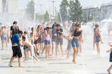 İzhevsk, Rusya - 20 Temmuz 2020: Mutlu çocuklar yaz parkındaki çeşmeye gülüp sıçrıyor. Bir grup çocuk şehir çeşmesinin derelerinde eğleniyor.