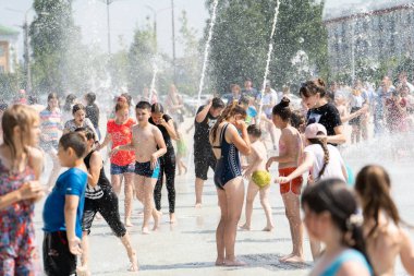 İzhevsk, Rusya - 20 Temmuz 2020: Mutlu çocuklar yaz parkındaki çeşmeye gülüp sıçrıyor. Bir grup çocuk şehir çeşmesinin derelerinde eğleniyor.