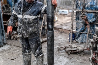 Kırmızı üniformalı, miğferli ve gözlüklü matkapçı. Petrol kuyusuna indirmek için matkap borularını vidalamak ve delmeye devam etmek için hidrolik anahtar kullanıyor. Çalışan insan kavramı.