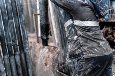 Kırmızı üniformalı, miğferli ve gözlüklü matkapçı. Petrol kuyusuna indirmek için matkap borularını vidalamak ve delmeye devam etmek için hidrolik anahtar kullanıyor. Çalışan insan kavramı.