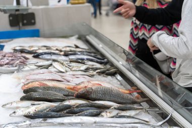 Yetişkin alıcılar balık dükkanının önünde ezilmiş buz üzerinde taze deniz ürünleri arıyorlar. Dondurucudan dondurulmuş yiyecek seçen bir kadın..