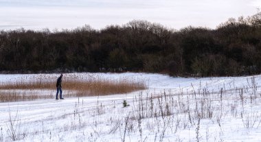 Donmuş gölde buz tutmuş bir ormanda kayan bir adamla güneşli güzel bir sabah. Görüntü Hollanda 'nın kuzeyinde çekilmiştir..