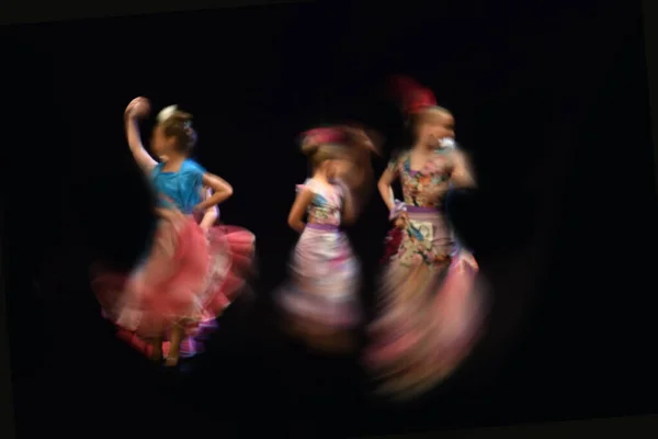 Flamenco dancers, spain. Blurred view of three dancing girls in folk dress on dark background.