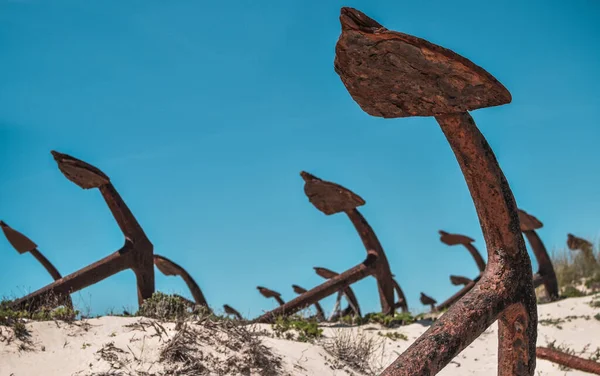 Anchor's cementary on the beach at Praia Do Barril in Santa Luzia, Algarve, Portugal. Old rusty marine anchors in dunes with blue sky.