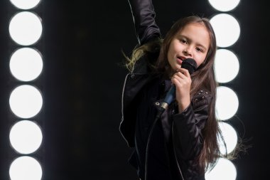 Sahne ışıkları önünde şarkı söyleyen küçük kız