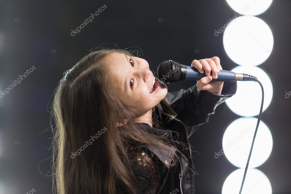 Little girl singing in front of stage lights