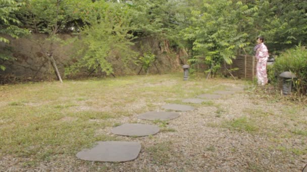 Азиатка в японском кимоно раздувает и спускается по тропинке в японском саду — стоковое видео