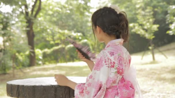 Mujer asiática en kimono japonés abanicándose en jardín de estilo japonés — Vídeo de stock