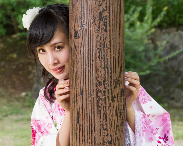 Asiatisk kvinna i kimono bakom trä pelare — Stockfoto