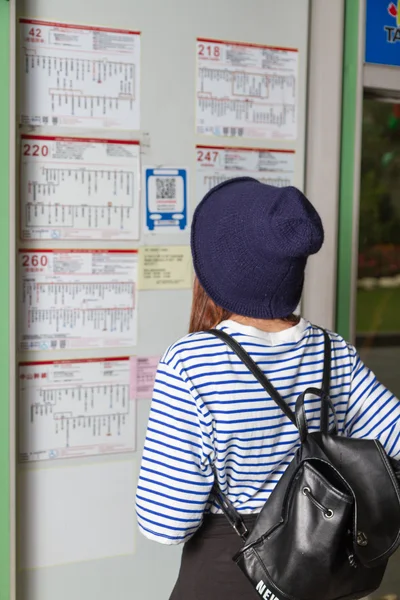 Kvinna vid busshållplats tittar på tidtabell — Stockfoto