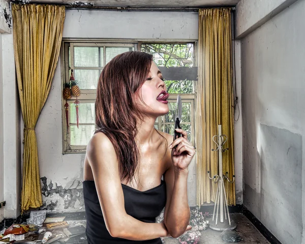 Chinese woman in abandoned aprtment about to lick a knife — Stock Photo, Image