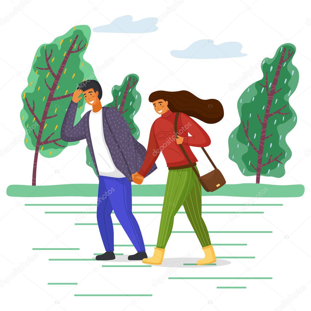 Woman and man in casual clothes walk in the park on the road along the tree alley in windy weather