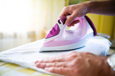 Erkek eli ütü masasında buhar ütüsüyle giysileri ütülüyor..