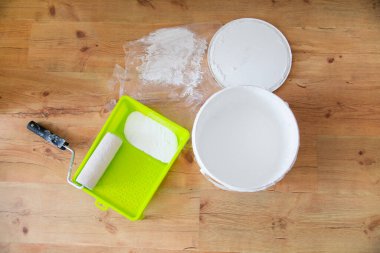 Ev boyama aletleri. Yeşil boya tepsisinde bir boya silindiri ve ahşap bir zeminde açık beyaz boya kutusu, üst manzara. Dairenin yenilenmesi, duvarların parlak bir kompozisyonda boyanması.