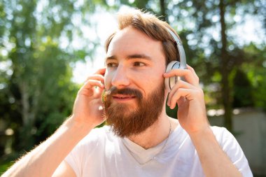 Genç adam, hipster kulaklıkla müzik dinliyor. Açık havada, müzikle rahatlıyor.. 