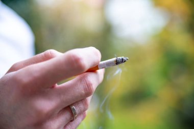 Sigara bağımlılığı. Erkek, dışarıda sigara tutuyor..