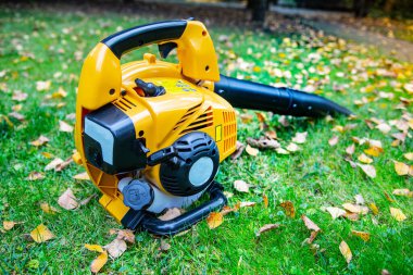 A close-up of an orange cordless, electric leaf blower lying on a grass. Autumn, fall gardening works in a backyard, on a lawn. Garden works.