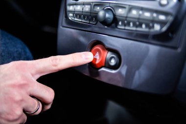 Male hand pressing a hazard warning lights button with a red triangle on a car dashboard. A road accident, a car breakdown, emergency situation.