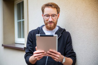 Evin dışında tablet kullanırken gülümseyen genç bir adamın ön görüntüsü..