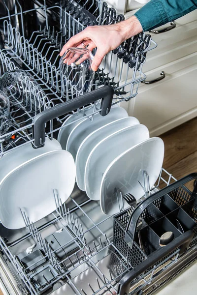 남자 손이 탁트인 식기세척기에서 깨끗 한 유리를 꺼내고 있다. 현대식 주방 기구를 가지고 집안 일을 한다. — 스톡 사진
