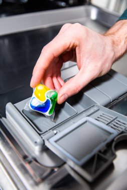 Erkek el bulaşık makinesine deterjan koyuyor..