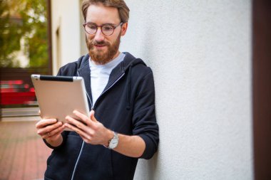 Man smiling while using a tablet outdoor, outside the house. Using an electronic, mobile, portable device to browse the internet, to read books, newspaper.