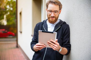 Evin dışında tablet kullanırken gülümseyen genç, sakallı bir adam. İnterneti gezmek, kitap okumak, gazete okumak için elektronik, mobil, taşınabilir bir cihaz kullanıyor..