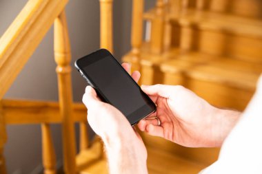 A mobile phone with a blank touchscreen with a copy space in male hands. Using an electronic, mobile, portable device, a smart phone at home.