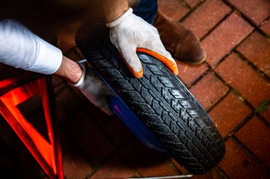 Horizontal view of male hands holding a spare wheel, an emergency warning triangle in a background. Changing a car tyre at night.