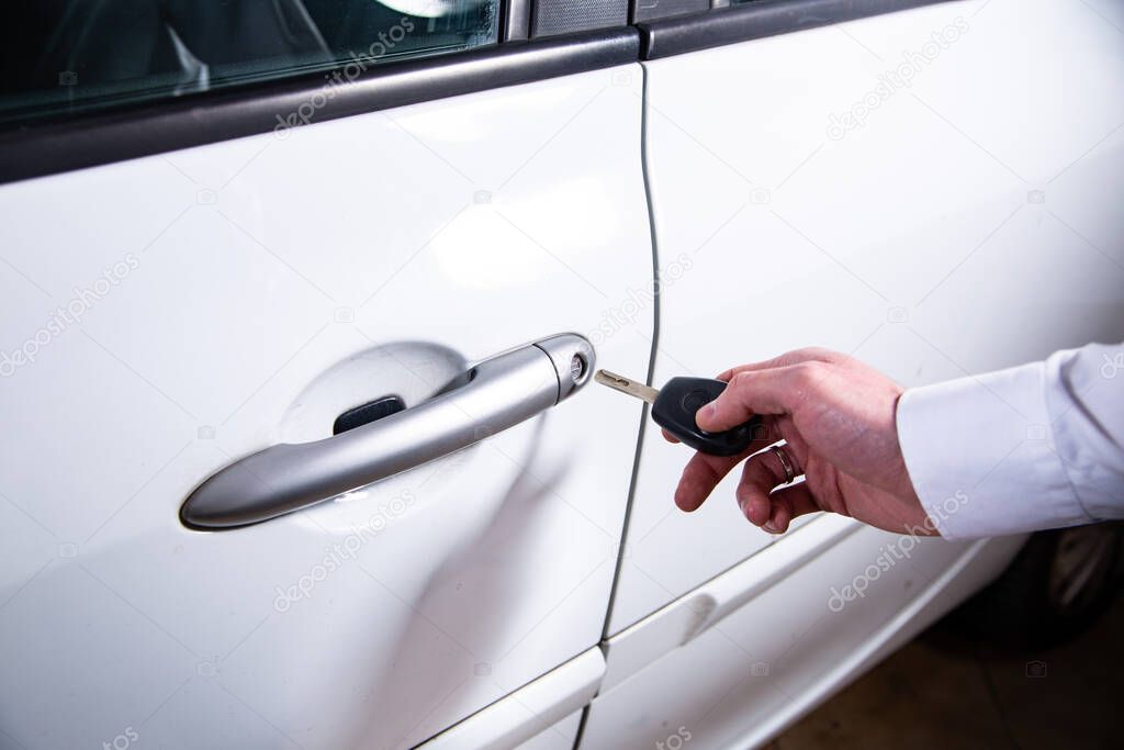 Male hand holding a spare key for emergency opening a car door of a silver car.