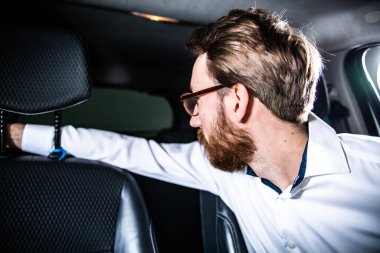 Man reversing a car by turning around in driver seat and laying right arm along the top of the passenger seat. Driving a car, parking.