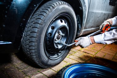 Male hands holding and using a lug wrench to unscrew lug nuts on the wheel, selective focus. Changing a car tyre at night.