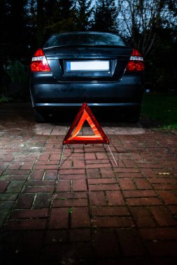 An emergency warning triangle placed behind a black car. A road accident, a car breakdown.