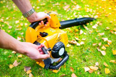 Starting a handheld, cordless, electric leaf blower in a garden. Autumn, fall gardening works in a backyard, on a lawn, grass. Garden works. 
