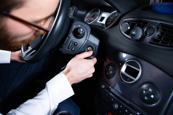 Man starting a car engine with an ignition key. Putting a key into the ignition to start an auto, a vehicle. 