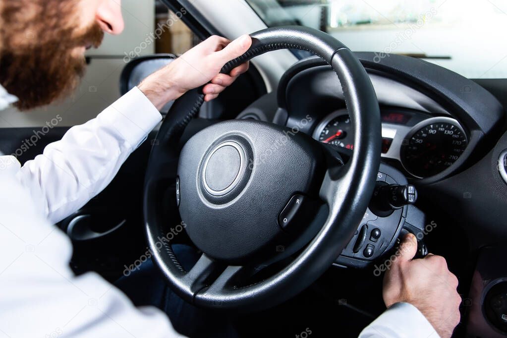 Driver holding a steering wheel and starting an auto with an ignition key. Putting a key into the ignition to start the car engine. 