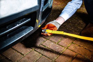 A male hand in a glove attaching a towline to a car, selective focus. Towing a broken vehicle with a tow rope.
